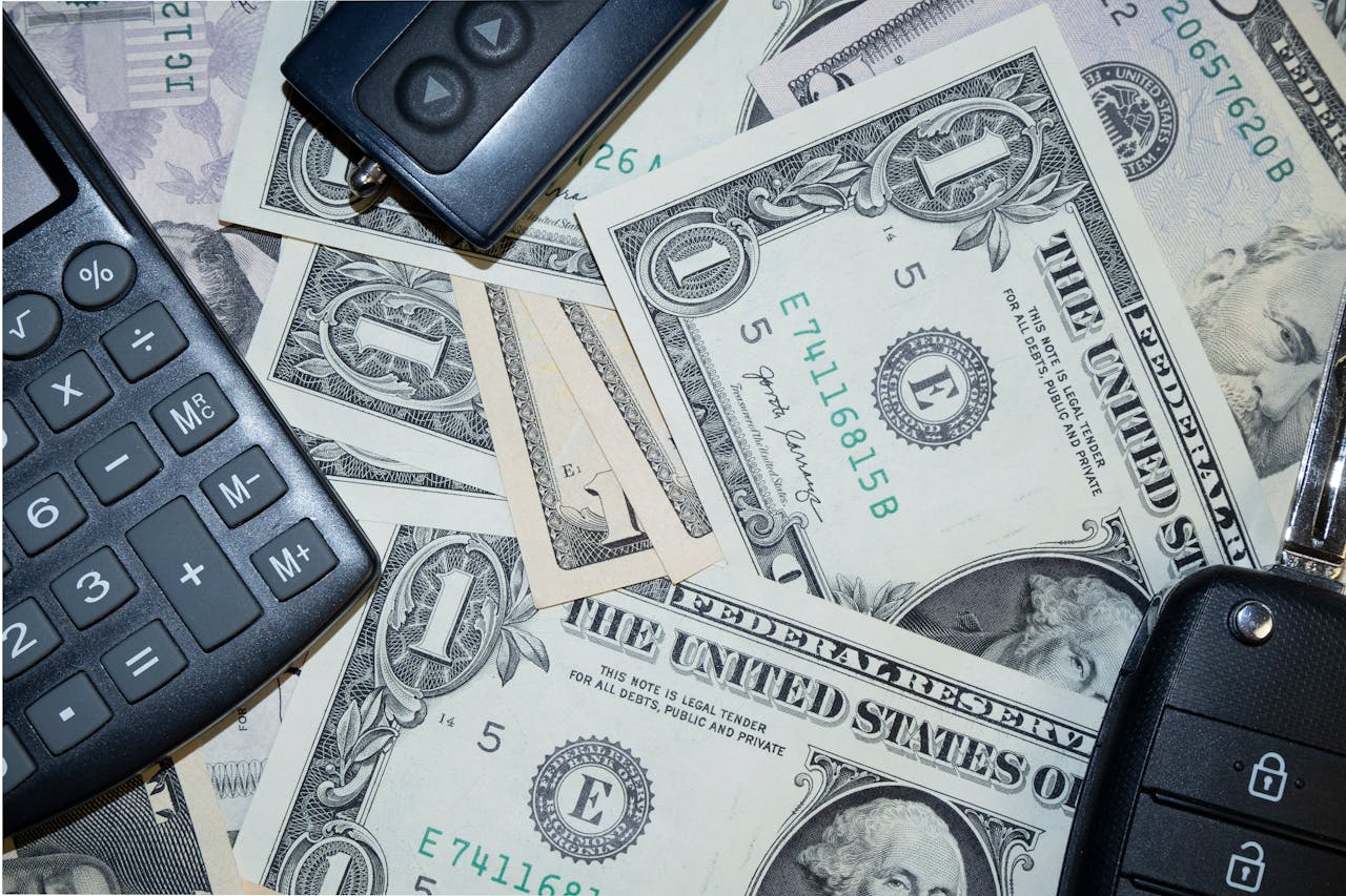 hero-img-01 An arrangement of US dollar bills, car keys, and a calculator representing finance and investment concepts.