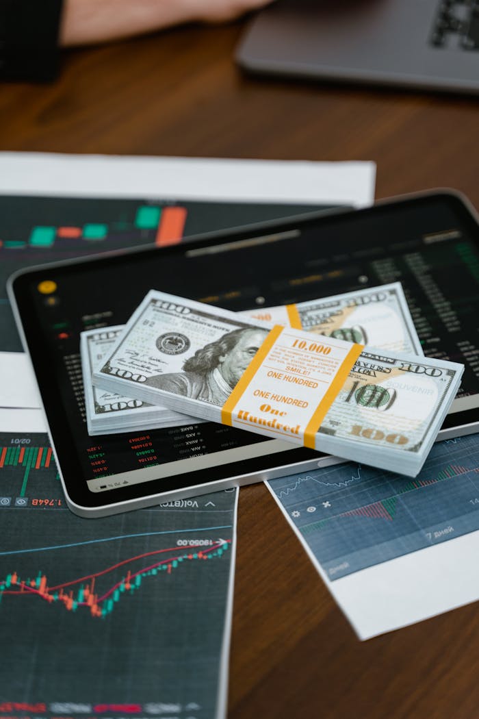 about-01 Stack of 00 bills placed on a tablet with financial graphs, symbolizing digital finance.